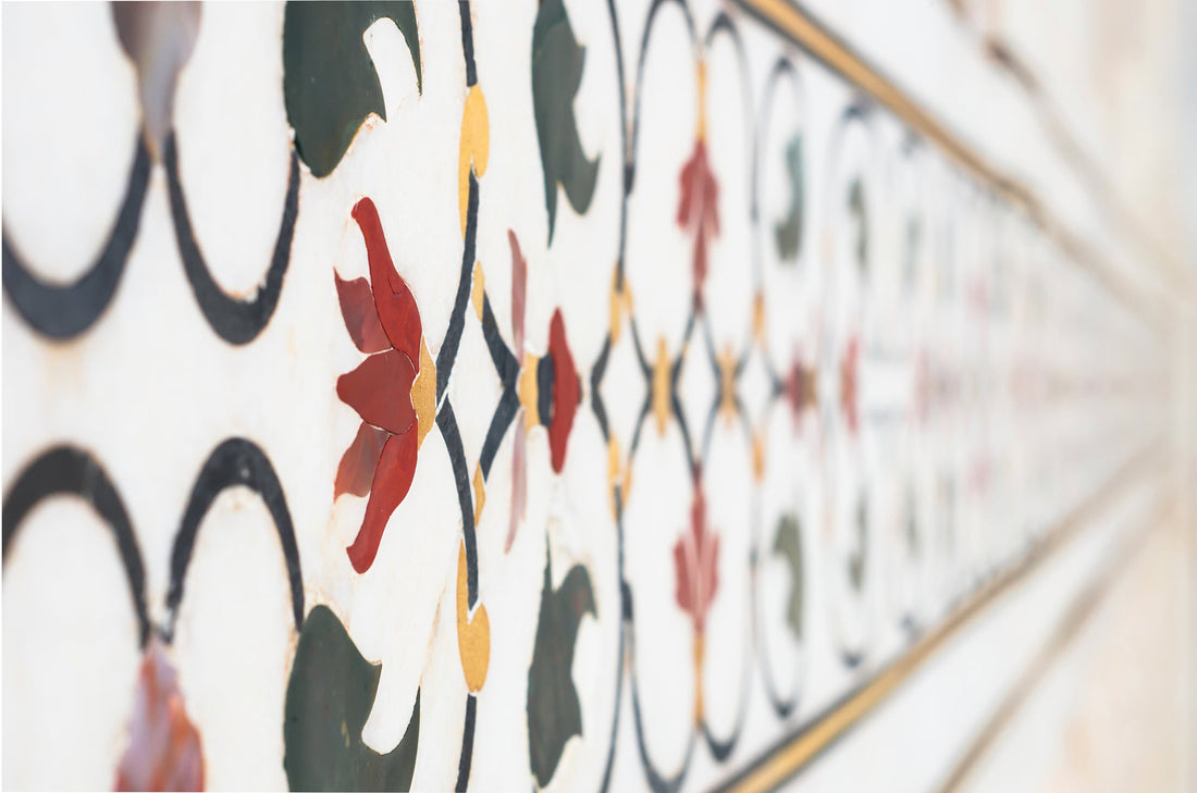 Close-up of floral pietra dura inlay in white marble, the border receding along a wall in perspective